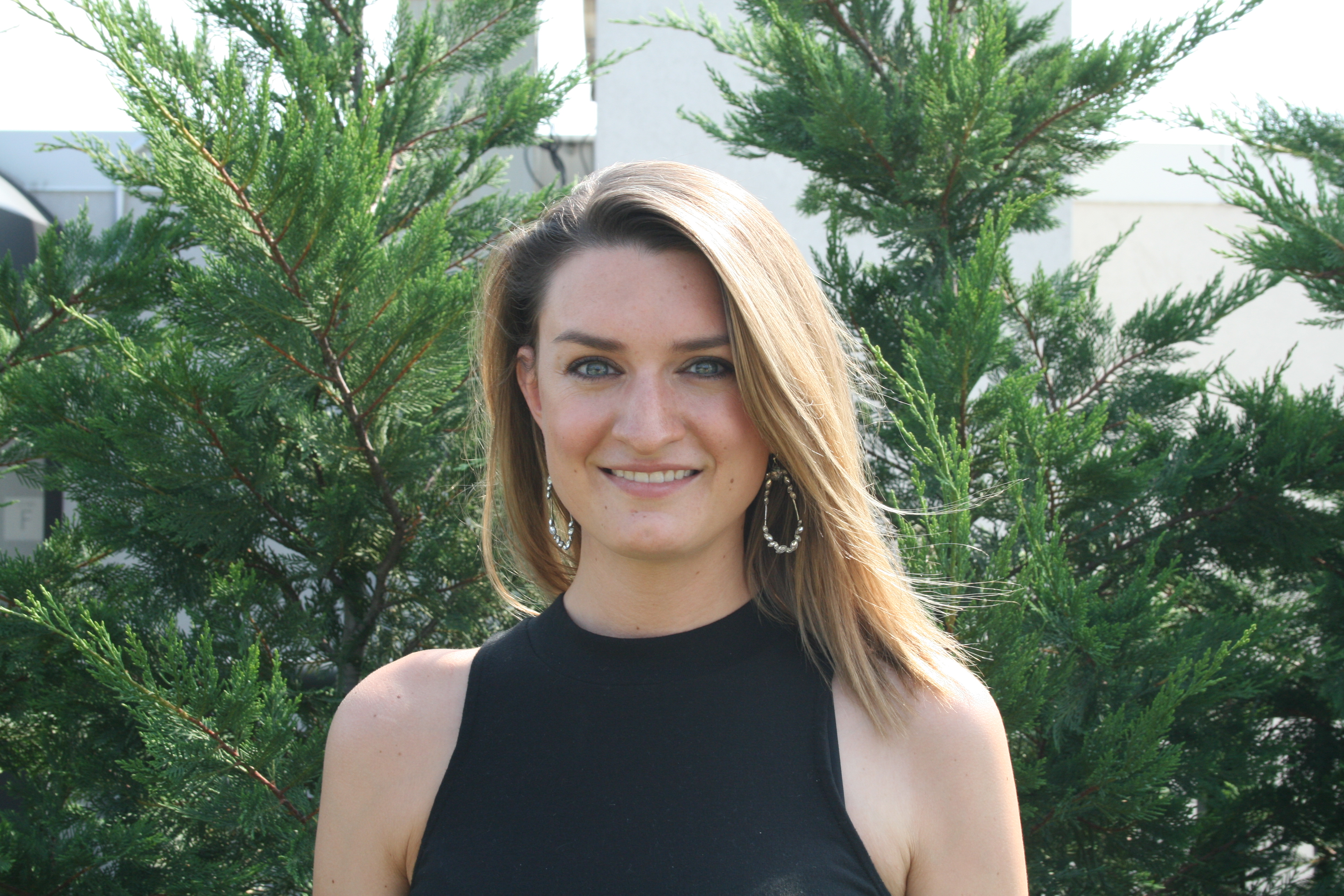 Danielle Newport Fancher, smiling, standing in front of a cypress hedge