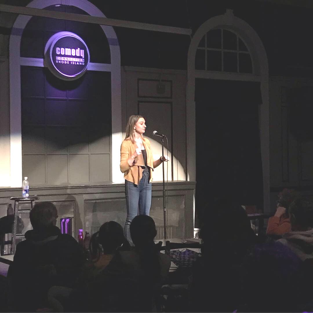 Danielle speaking to a seated audience under a spotlight