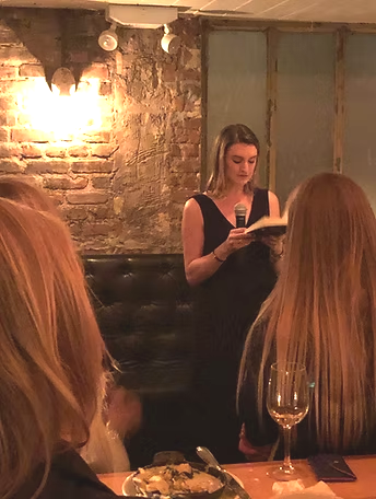 Danielle Newport Fancher reading aloud from 10 at her New York book launch, guests seated at candlelit tables around her
