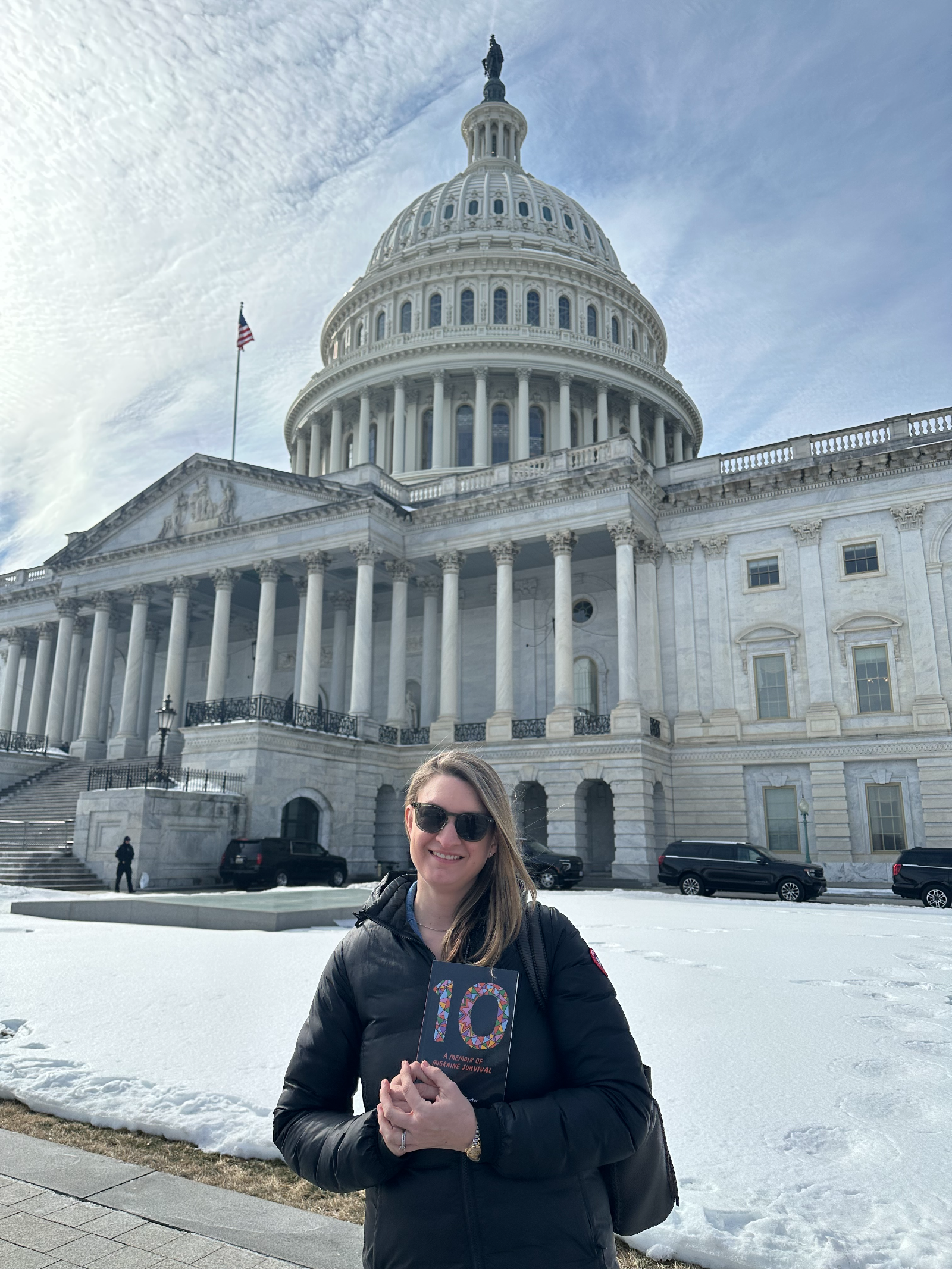 Danielle Newport Fancher standing in front of the United States Capitol holding a copy of 10: A Memoir of Migraine Survival