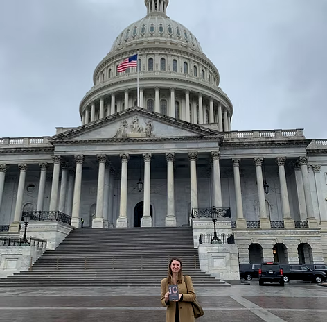 Danielle Newport Fancher holding a copy of 10 in front of the United States Capitol