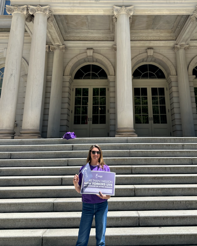 Danielle holding a Headache in the City sign on the steps of New York City Hall