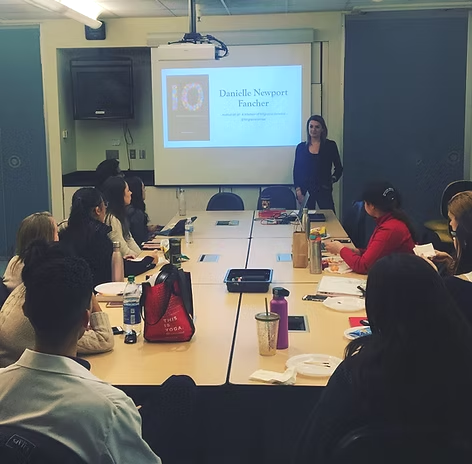 Danielle presenting to clinicians around a conference table, the cover of 10 projected behind her