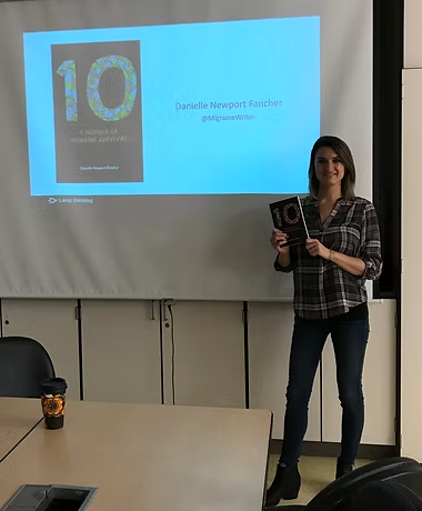 Danielle presenting in a lecture room, holding a copy of 10 beside a projected title slide